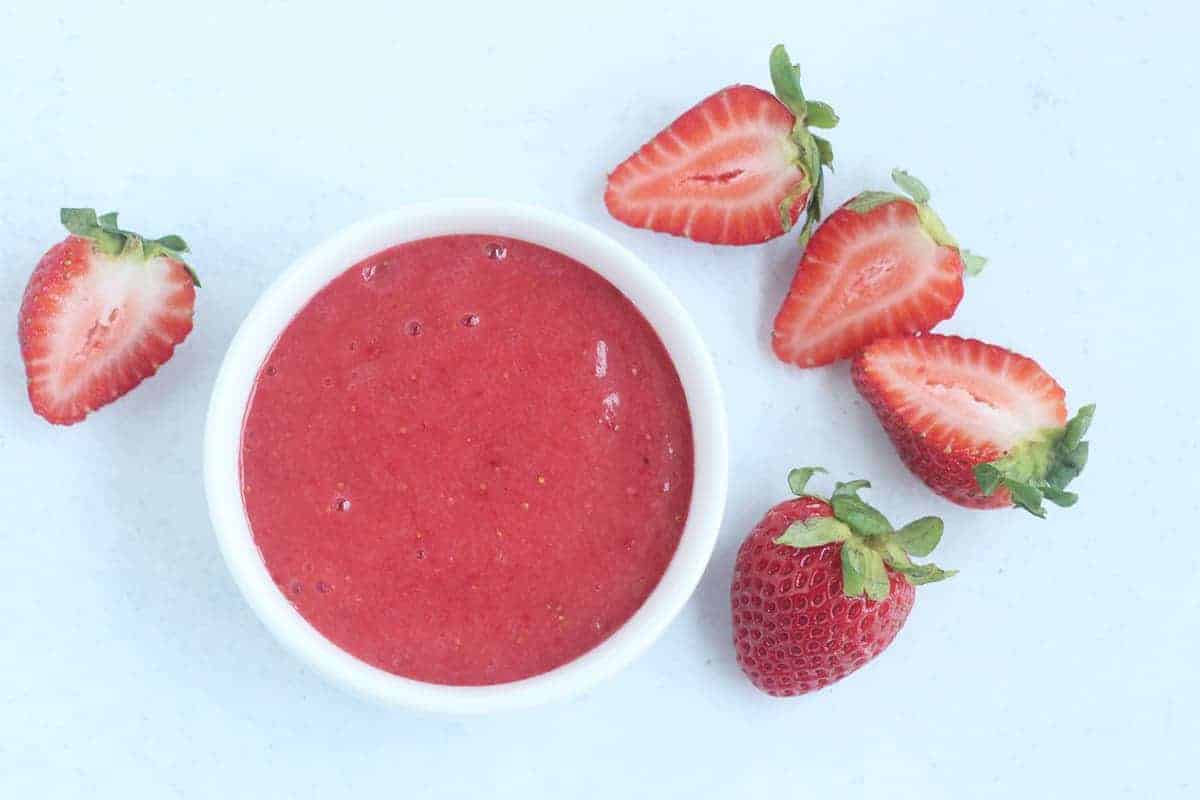 strawberry puree in white bowl with sliced strawberries on side