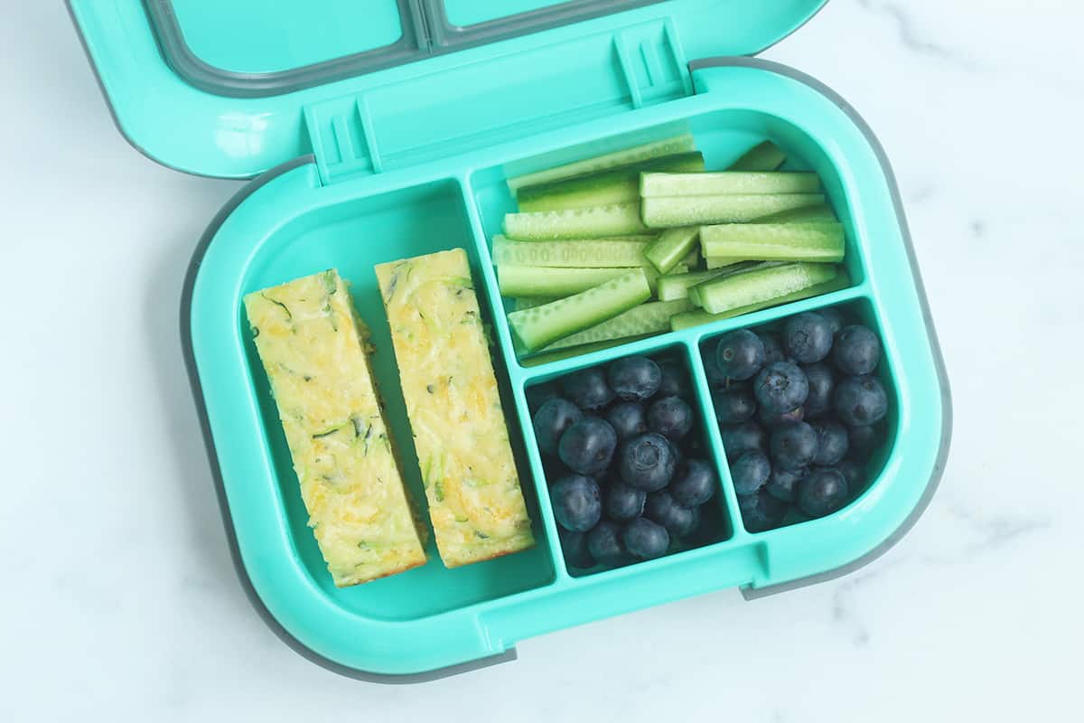 zucchini slice in kids lunchbox with blueberries and cucumbers
