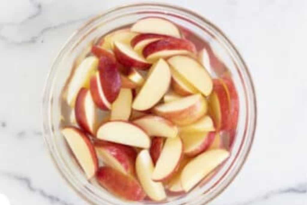 Apple slices in glass bowl covered with water.