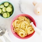 buttered noodles in kids bowl with cucumbers and cup on side