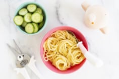 buttered noodles in kids bowl with cucumbers and cup on side