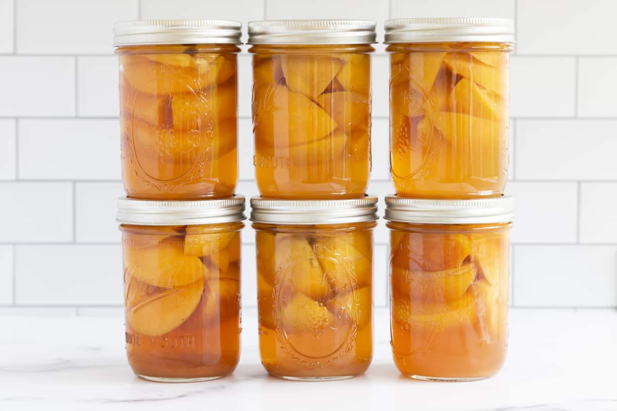 Stacked mason jars of canned peaches on white countertop