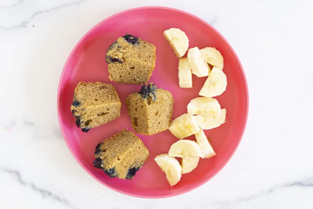 peanut butter muffin cut in quarters with banana on pink plate