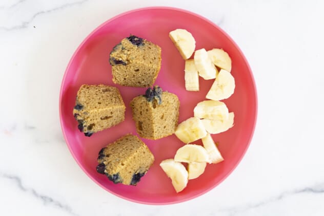 peanut butter muffin cut in quarters with banana on pink plate