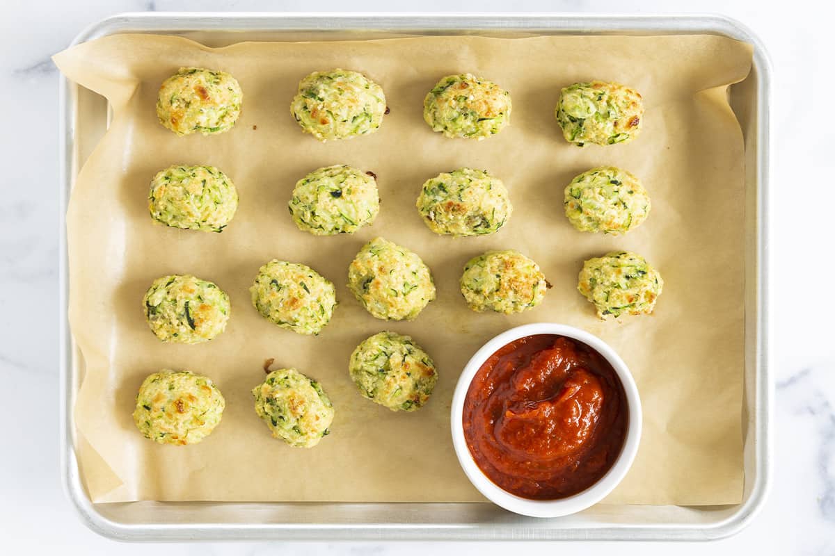 zucchini tots on parchment paper after baking with marinara sauce