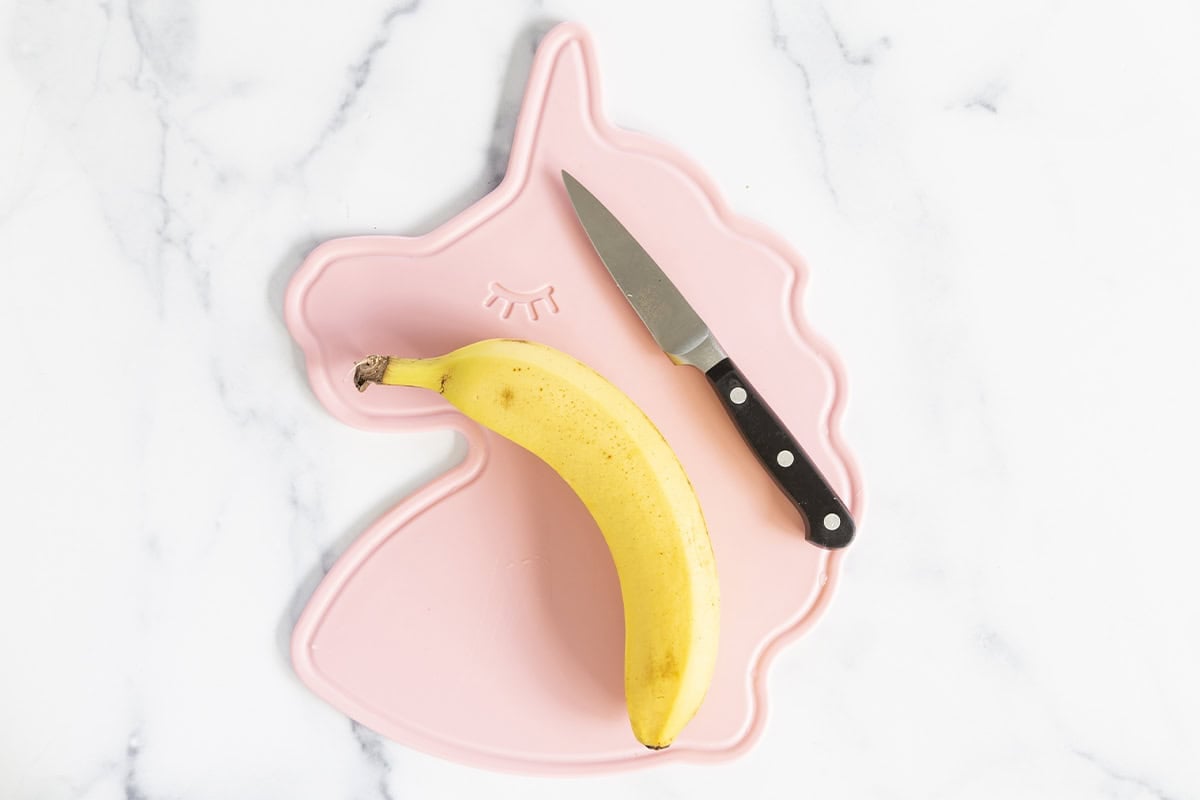 Banana with knife on cutting board.