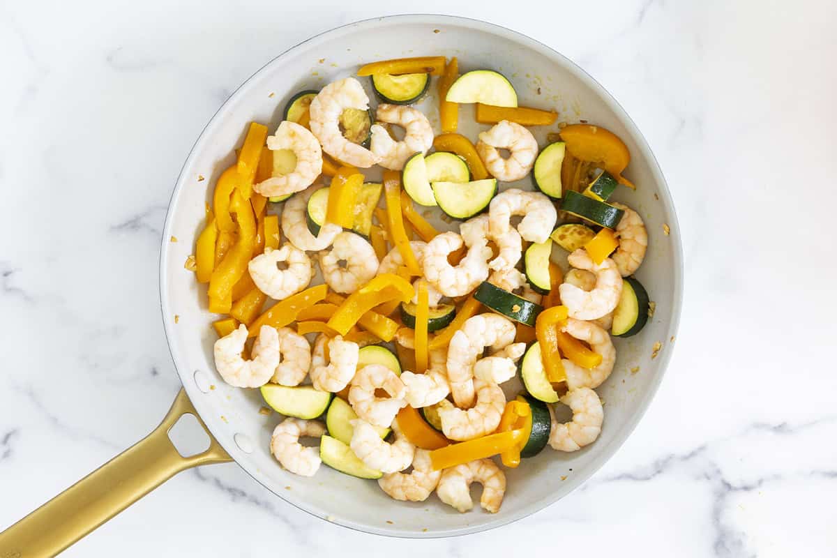 Cooking shrimp with veggies in pan.