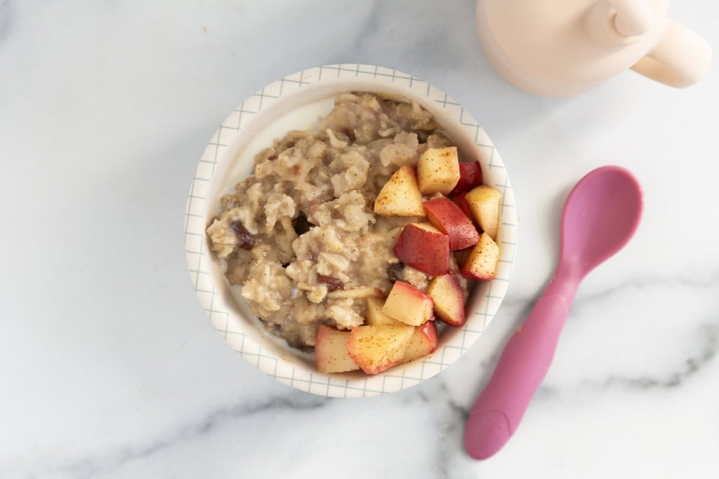 Apple cinnamon oatmeal in white bowl with spoon on side.