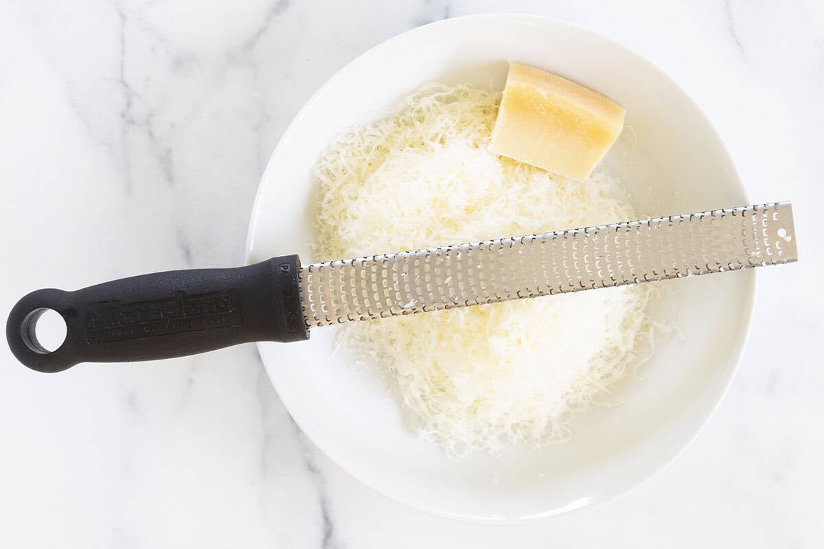 Grating cheese into white bowl for buttered pasta. 