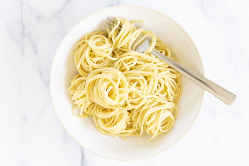 Buttered noodles in white bowl with fork.