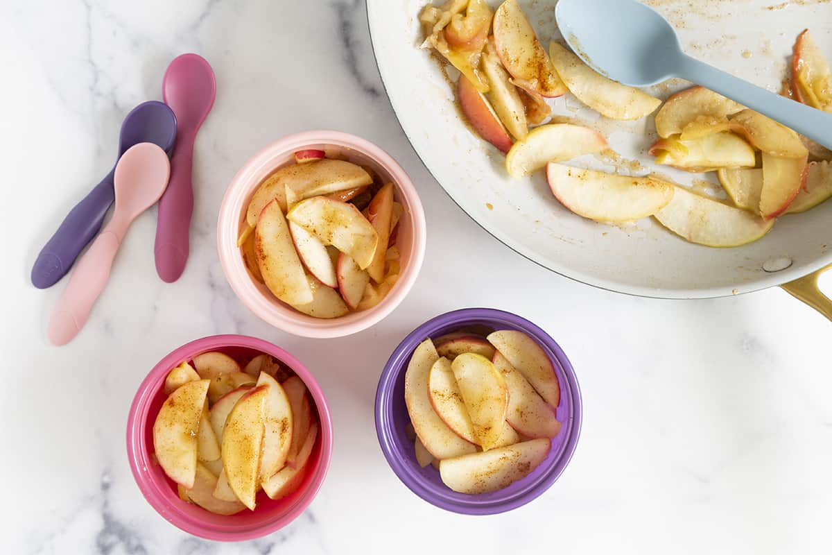 cinnamon apples in three bowls and pan with spoons.