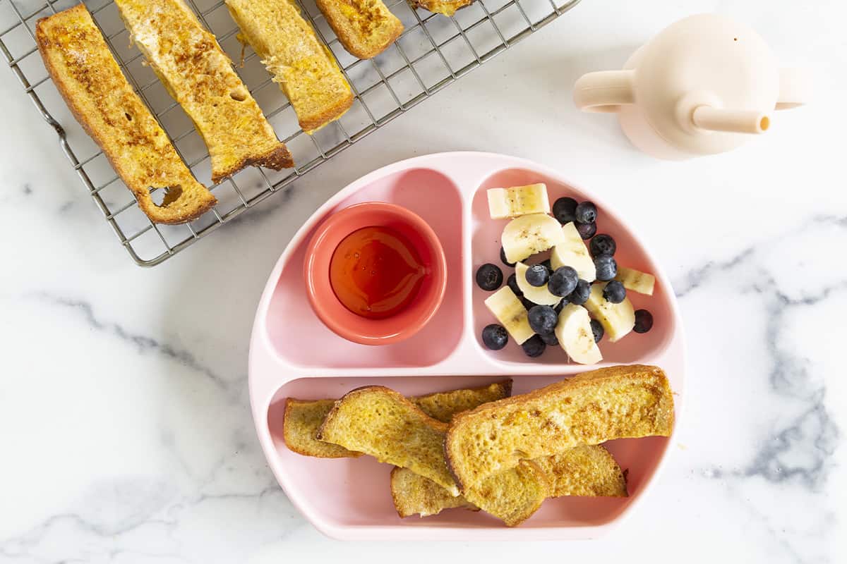French toast sticks on kids plate with sides.