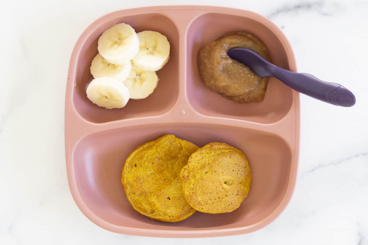 pumpkin pancakes on pink kids plate with banana slices.