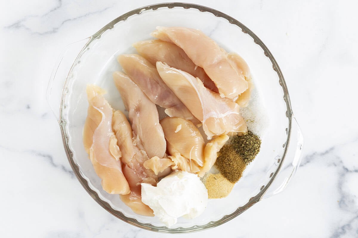 Chicken and seasonings in glass bowl for yogurt chicken. 