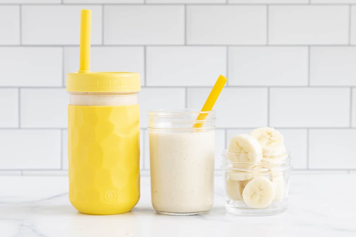 banana smoothie in two cups with sliced bananas in glass.