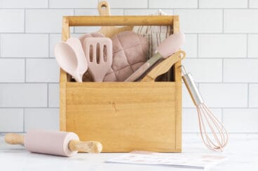 pink kids cooking set with wooden box on counter.