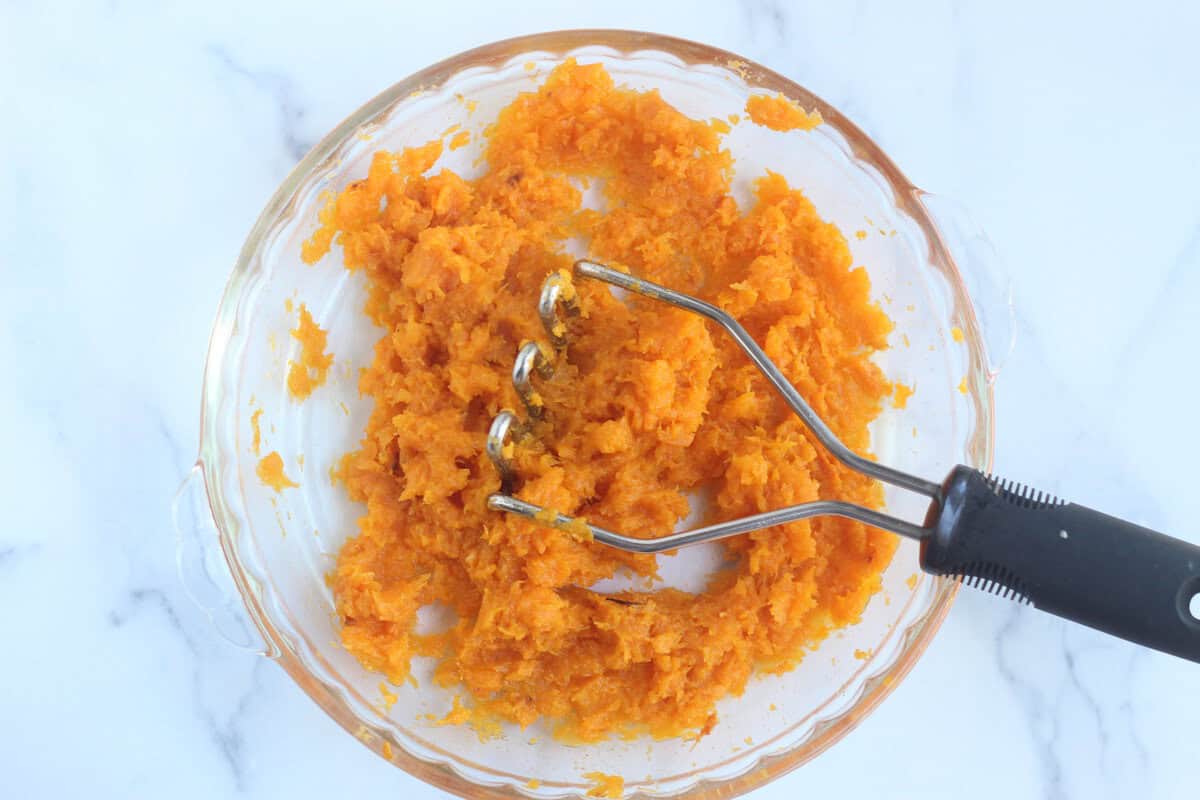Mashing butternut squash in glass bowl.