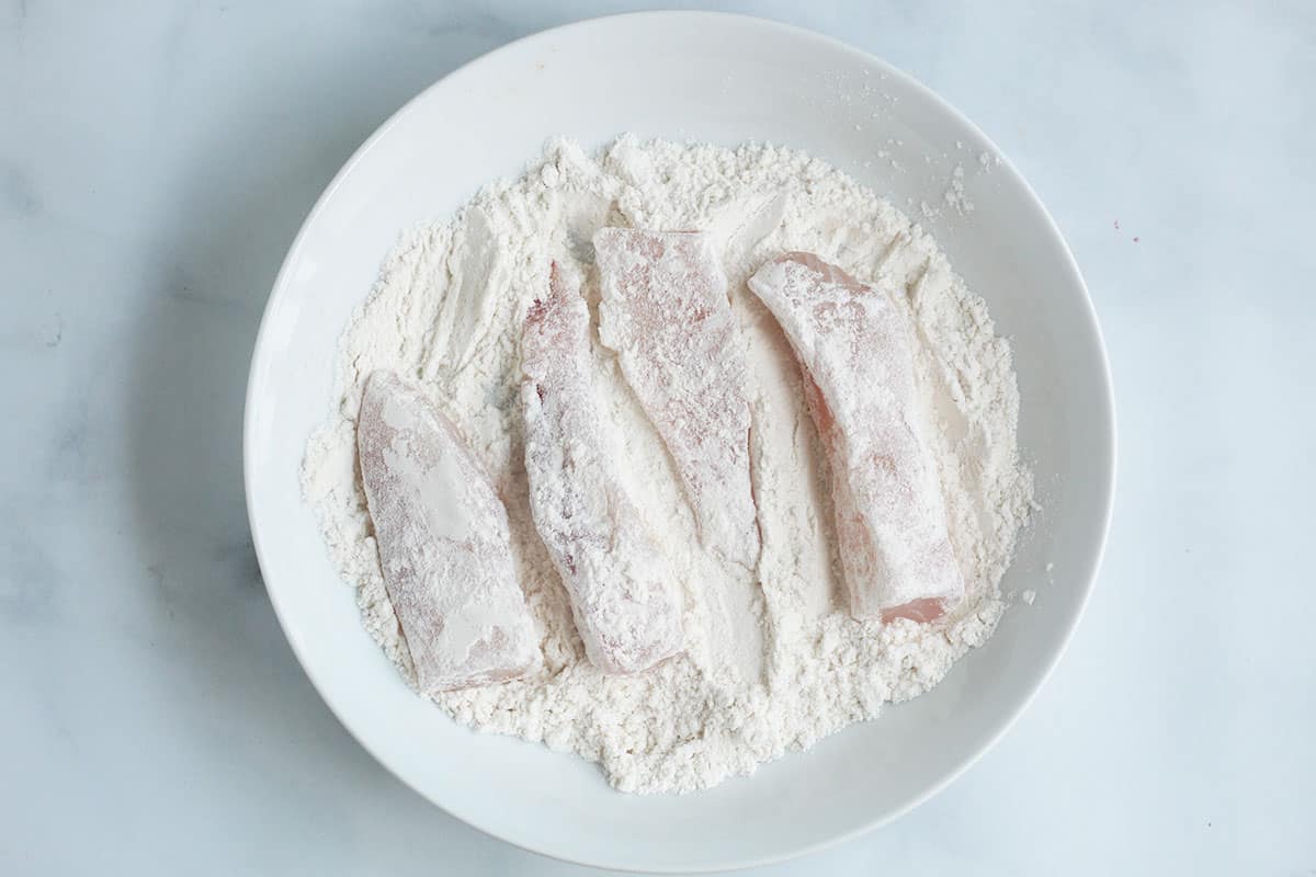 fish strips coated in flour in white bowl.