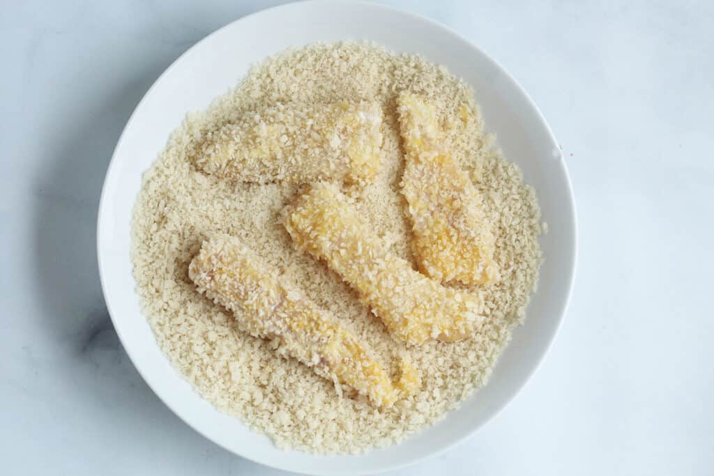 fish strips coated in breadcrumbs in white bowl.