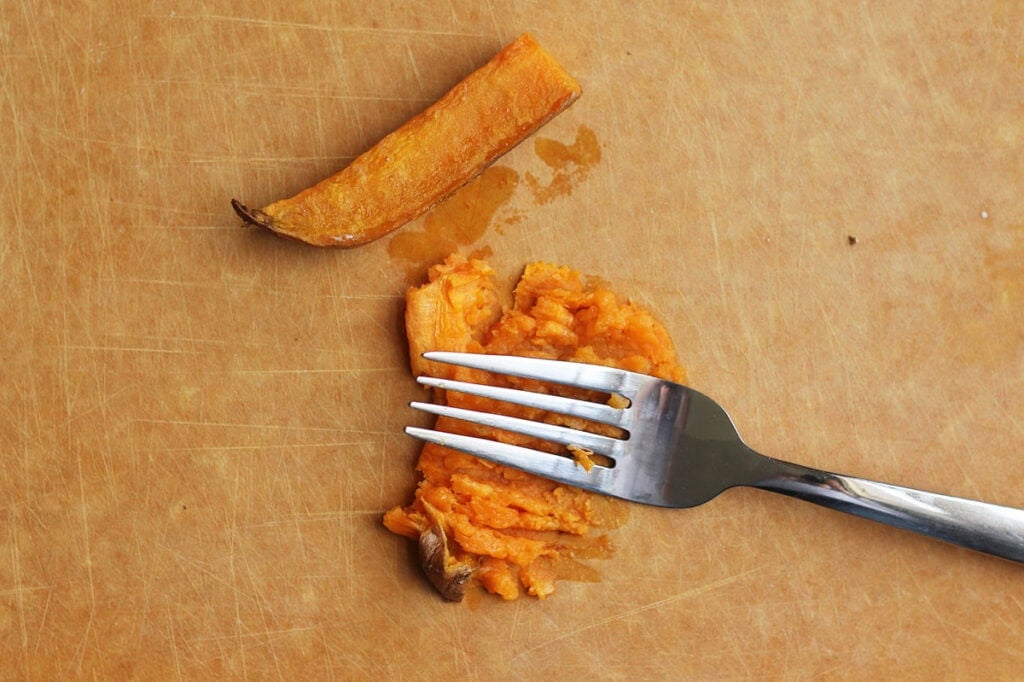 mashing sweet potato on cutting board.