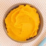 sweet potato puree in brown bowl with blue spoon.