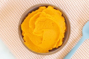 sweet potato puree in brown bowl with blue spoon.
