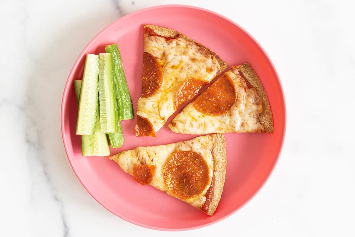Tortilla pizza on pink plate with cucumbers. 