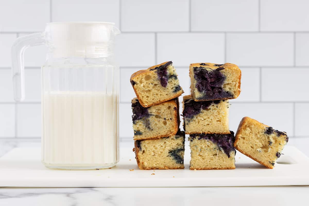 Blueberry yogurt cake pieces stacked with jug of milk.