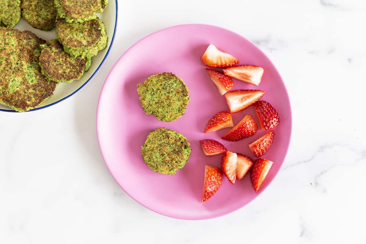 Broccoli fritters on pink plate with strawberries. 
