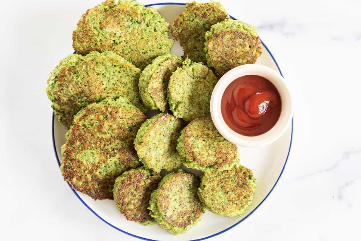 Broccoli fritters on white plate with dip on side.