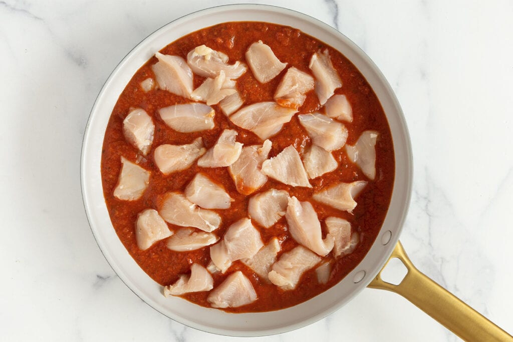 chicken pieces in marinara sauce in pan.