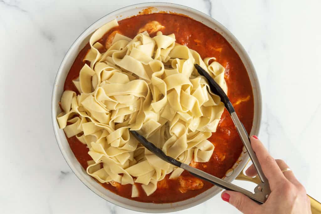 adding pasta to pan with marinara sauce and chicken.