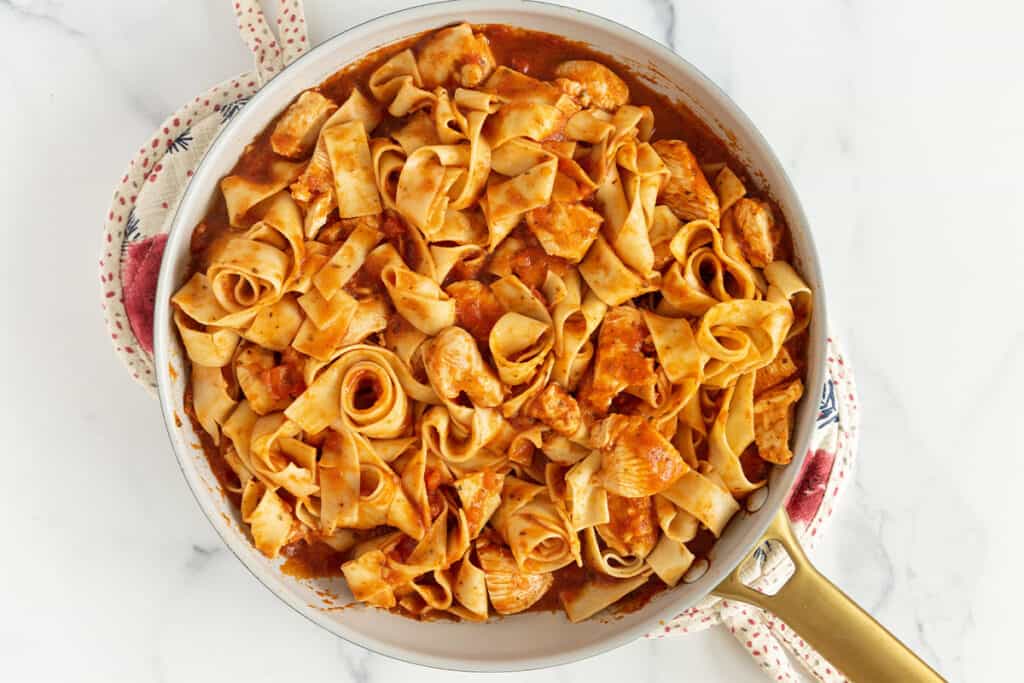pasta and chicken coated with marinara sauce in pan.