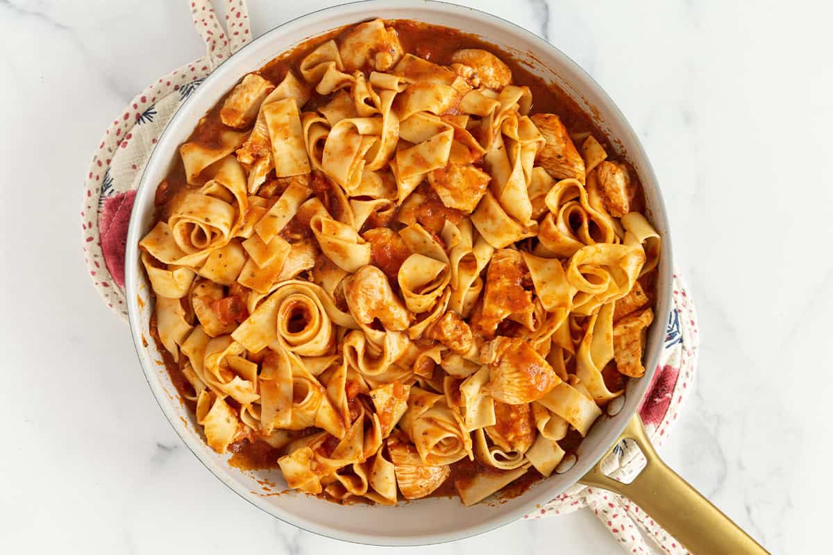 pasta and chicken coated with marinara sauce in pan.