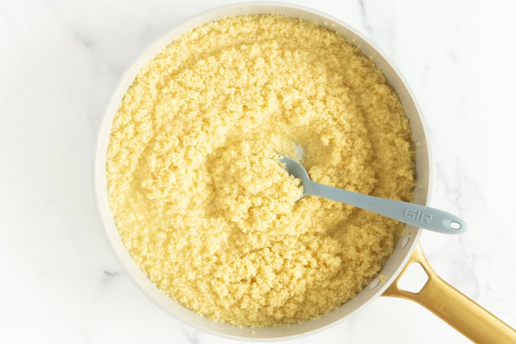Making pastina pasta in pot with blue spoon.