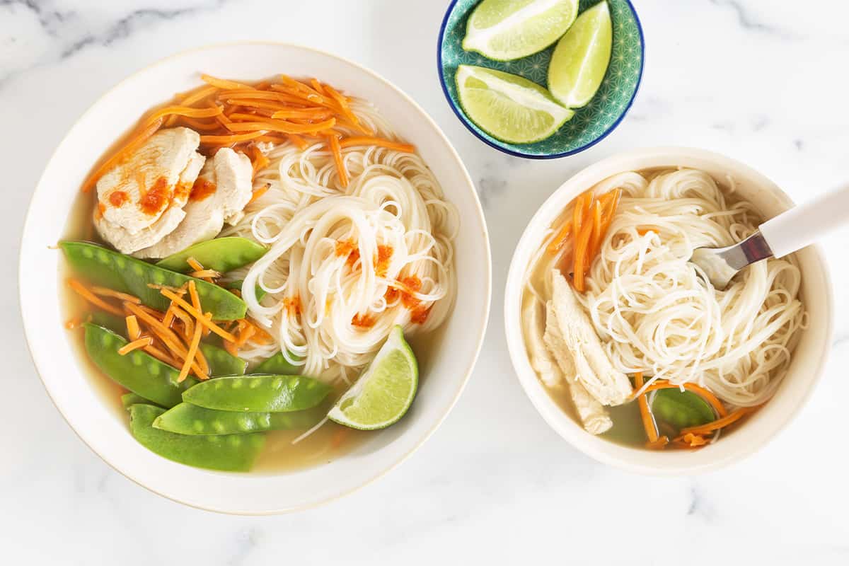 Rice noodle soup in two bowls with limes on side.