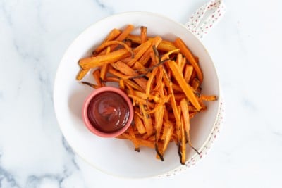 Air fryer roasted carrots on white plate with ketchup.