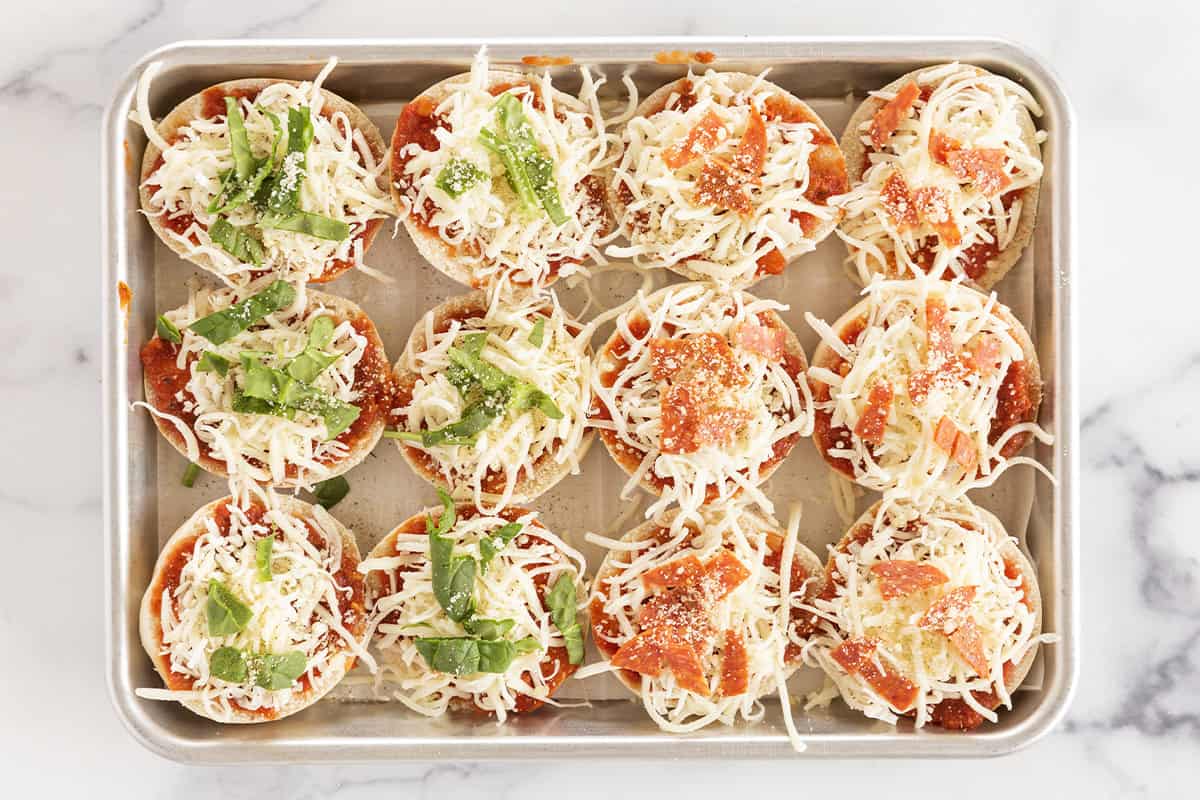 Adding toppings to bagel pizzas on sheet pan.