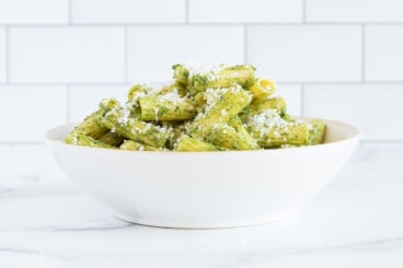 Green pasta sauce pasta in white bowl with cheese.