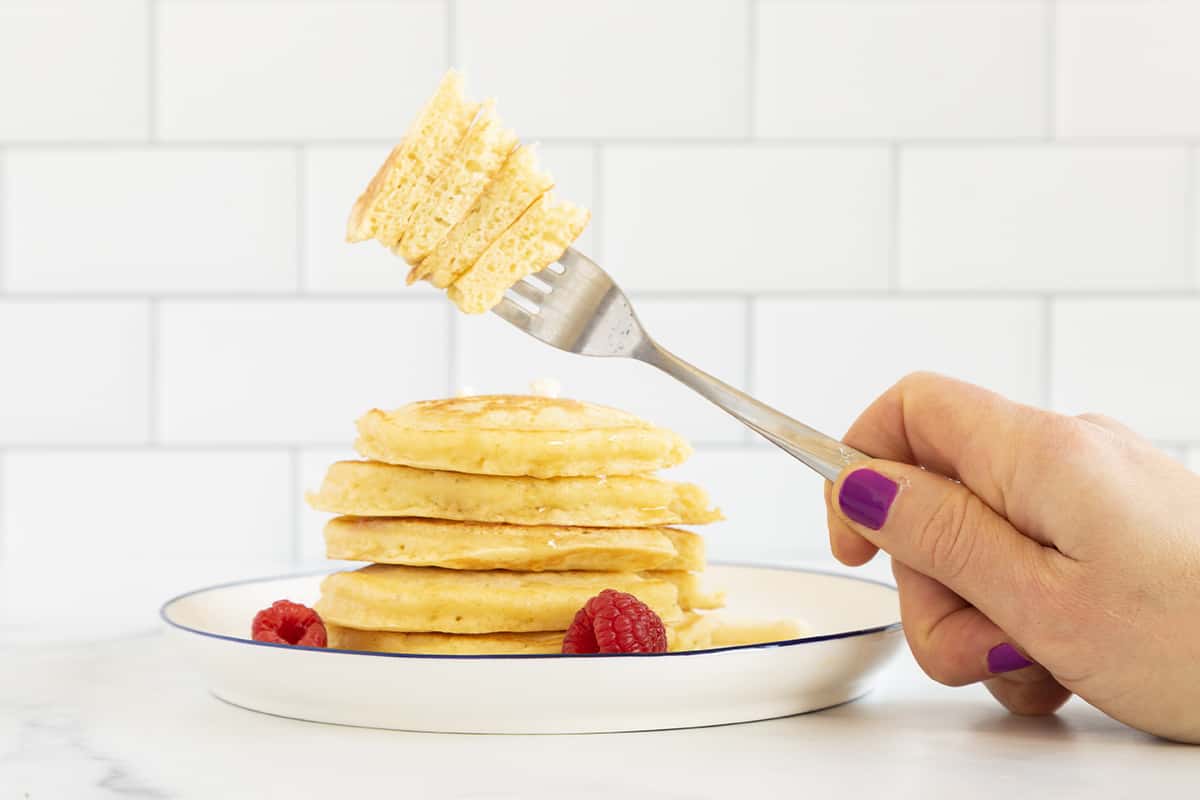 Fluffy ricotta pancakes in stack with hand holding fork.