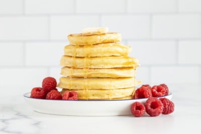 Fluffy ricotta pancakes in stack with syrup and raspberries.
