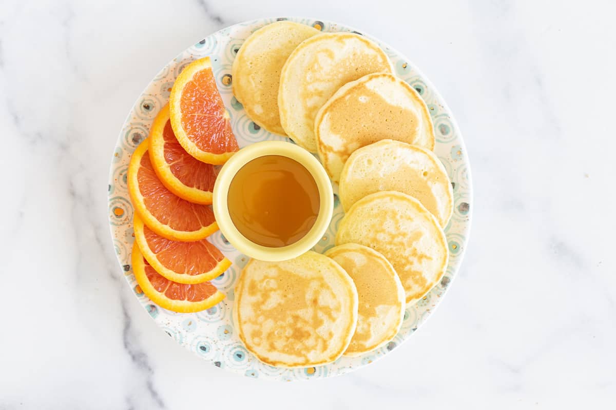 Silver dollar pancakes on plate with oranges.