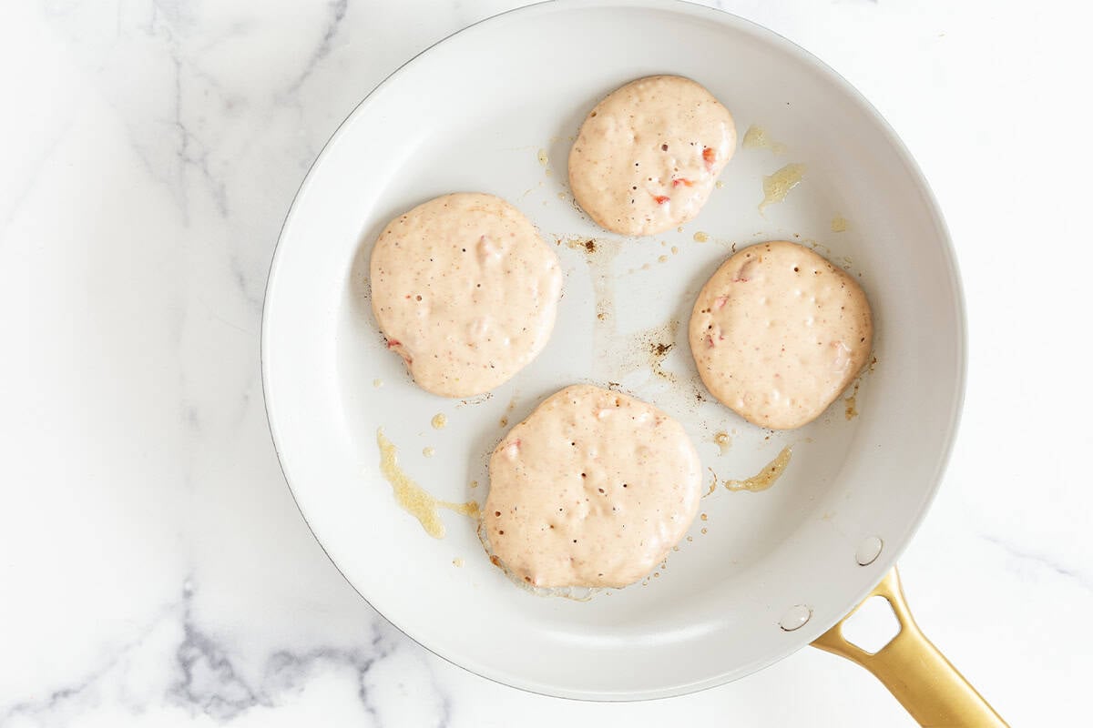 four strawberry pancakes cooking in white pan.