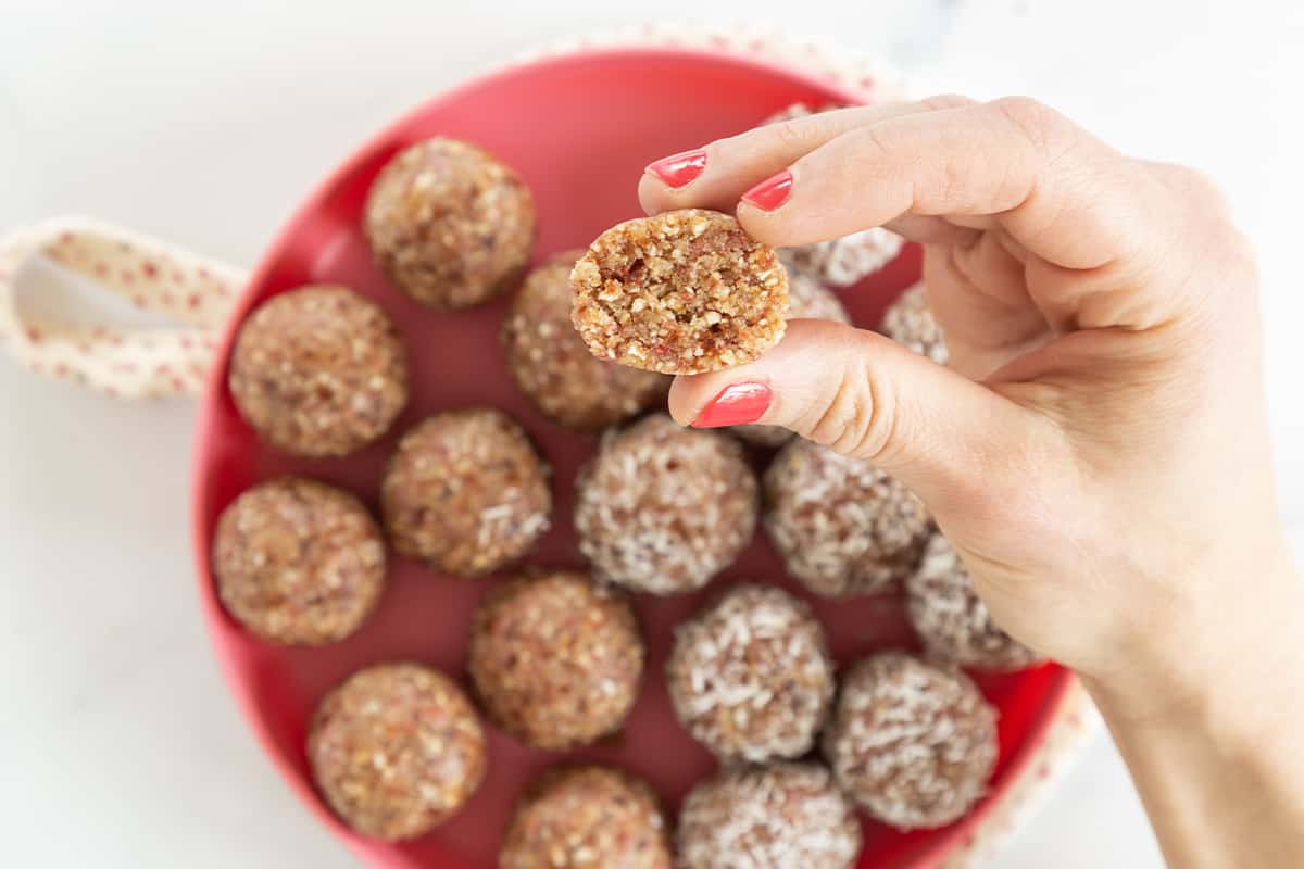 Bliss balls on red plate with hand holding one.