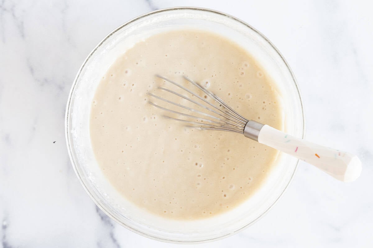 Batter for vanilla cake in glass bowl with whisk.