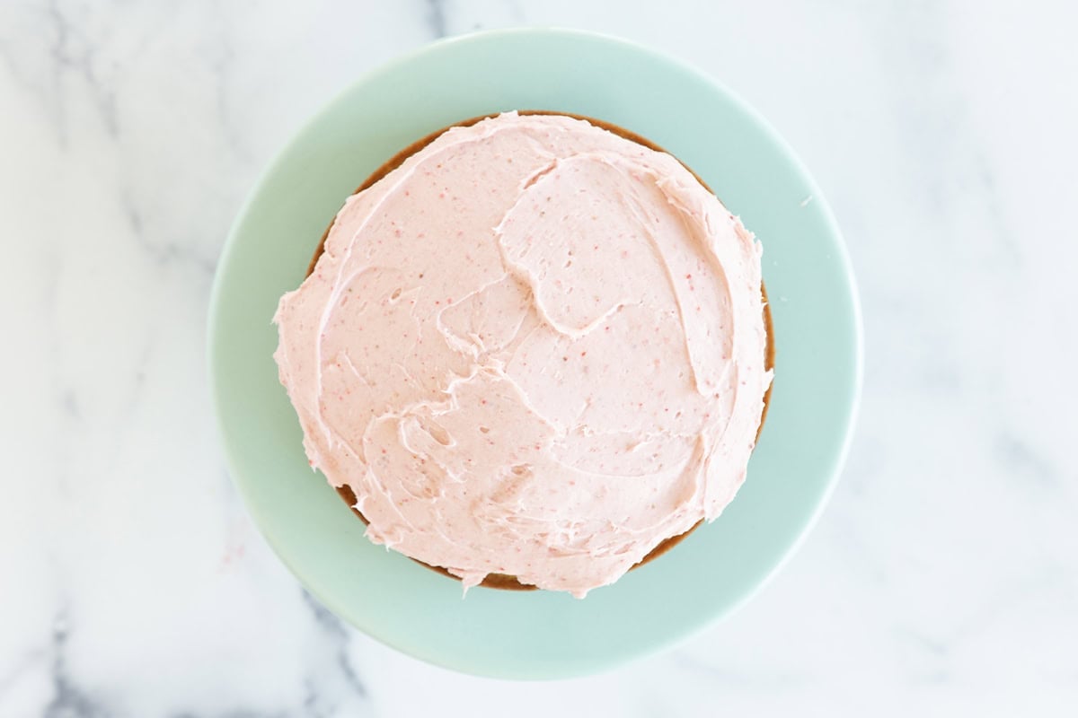 Frosting vanilla cake on blue plate.