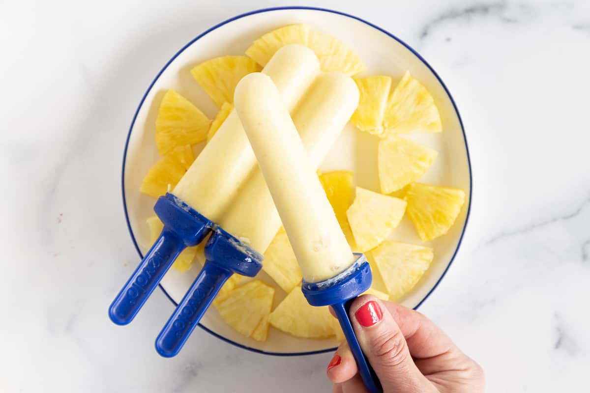 Hand holding pineapple popsicle.