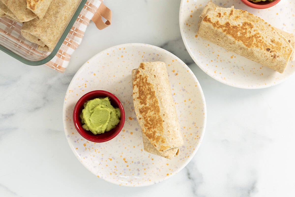 Rice and bean burritos on white plate with avocado on side.
