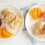 Rice and bean burritos cut in half on plates with oranges.