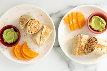 Rice and bean burritos cut in half on plates with oranges.